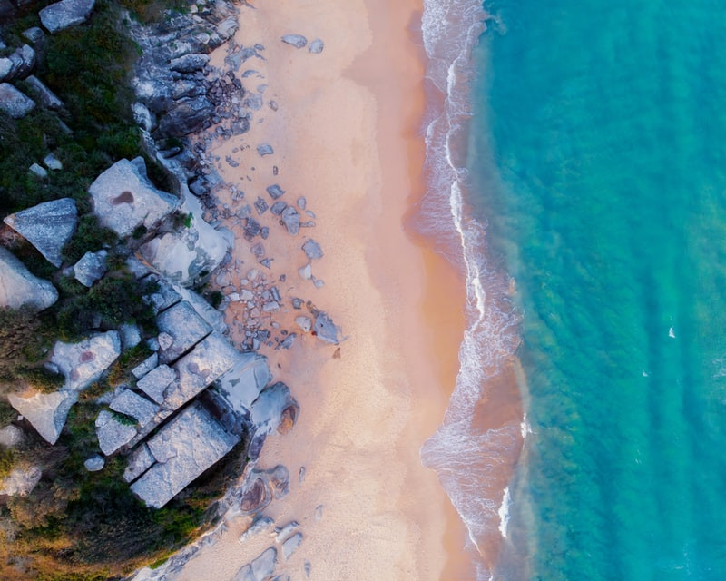 Aerial view of rocky coastline with sandy beach and blue sea